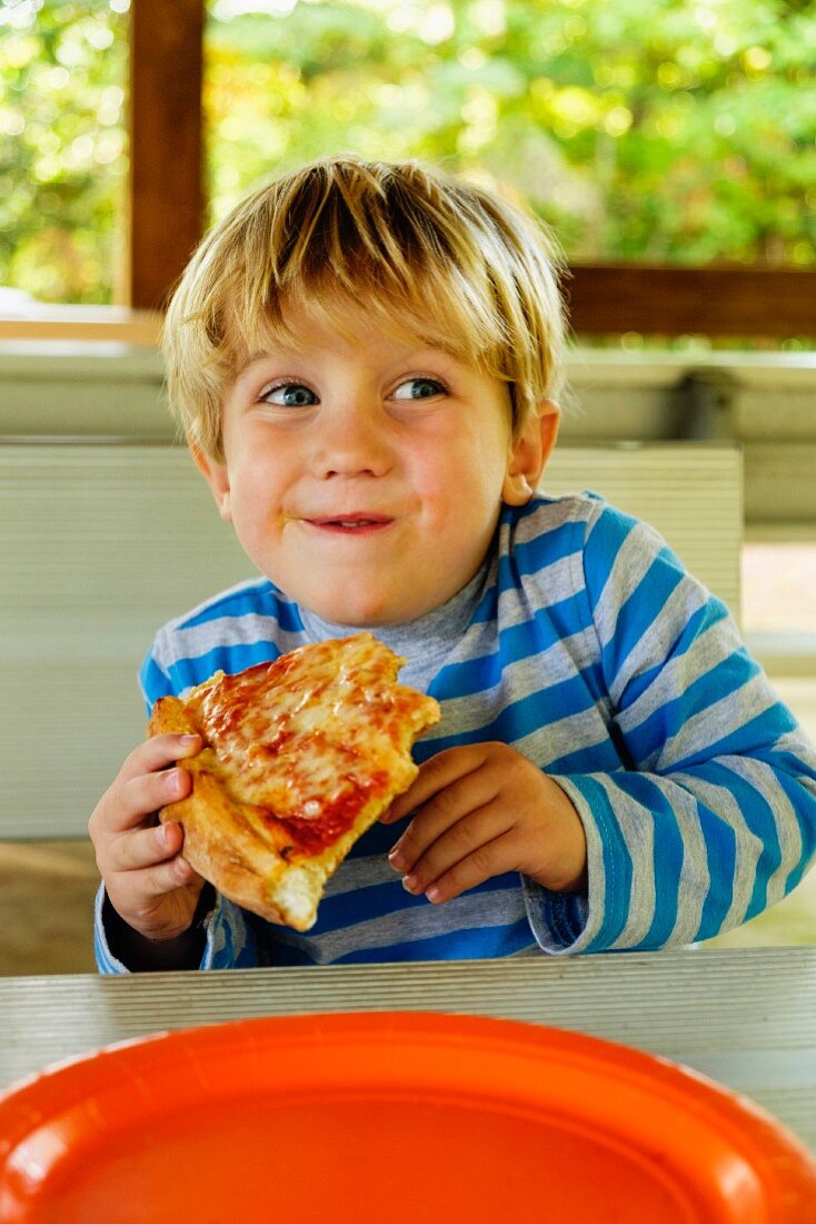 Blonder Junge isst ein Stück Pizza