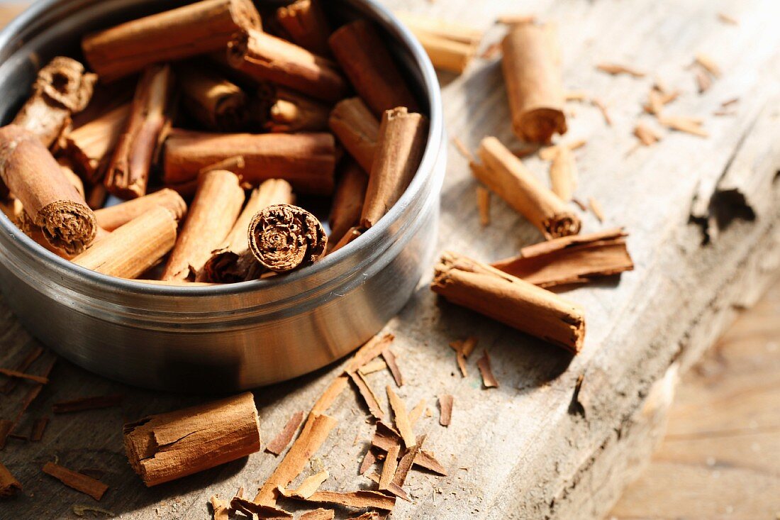 Cinnamon sticks inside and next to a tin on a wooden surface