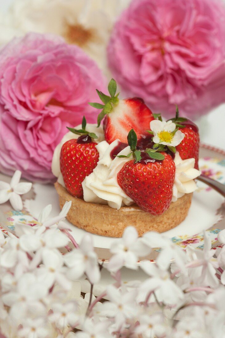 Strawberry cake with cream surrounded by summery roses and jasmine blossoms