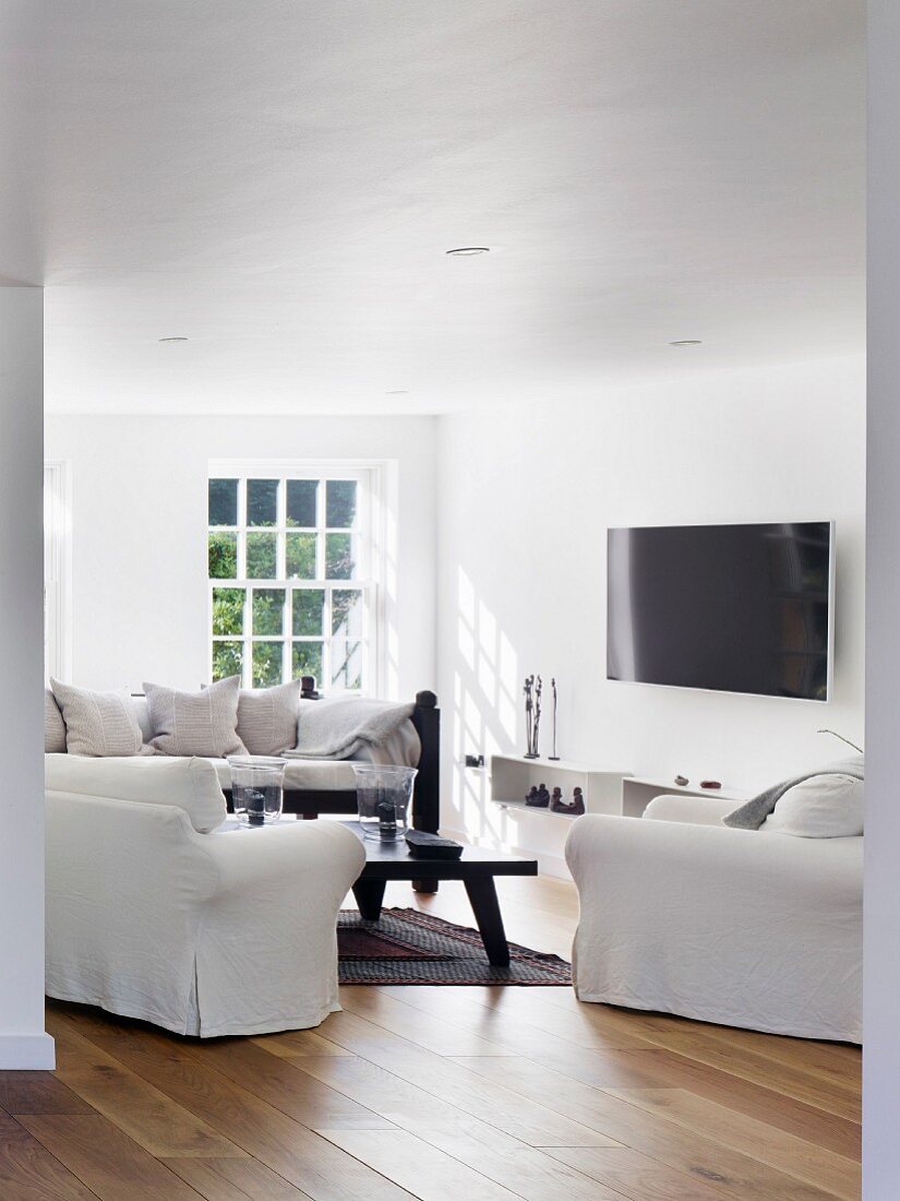 Weißer Loungebereich mit aufgehängtem Flachbildschirm und schwarzem Couchtisch