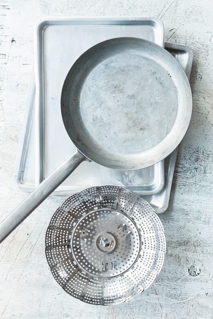 Kitchen utensils for different cooking methods: a pan, a baking tray and a steamer basket