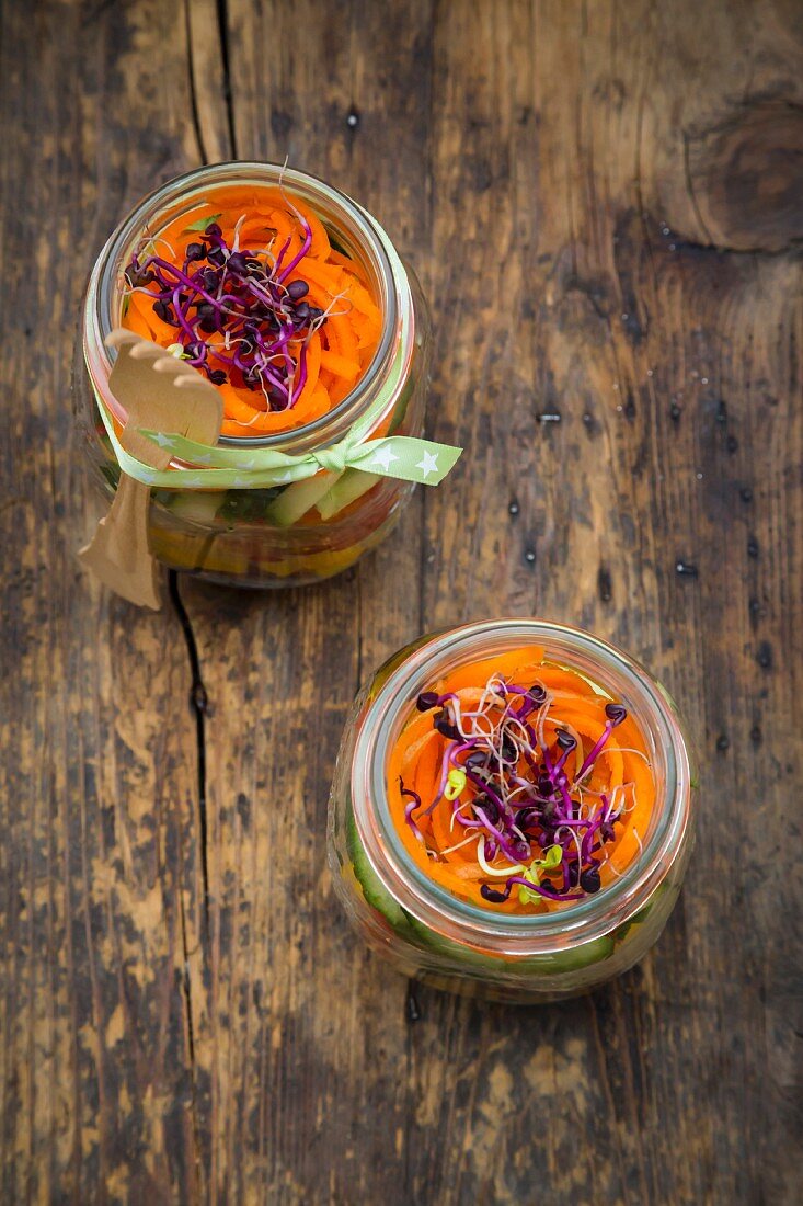 Rainbow salad in glass jars with red cabbage, yellow pepper, tomato, cucumber, carrots and beetroot sprouts