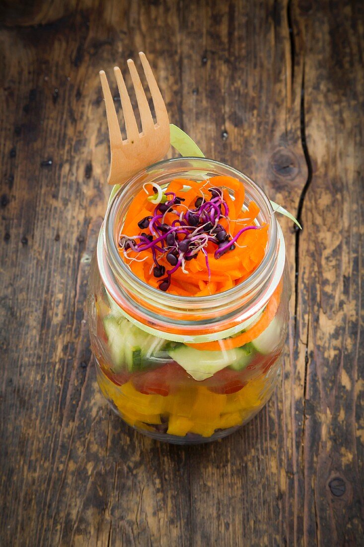 Rainbow salad in glass jars with red cabbage, yellow pepper, tomato, cucumber, carrots and beetroot sprouts