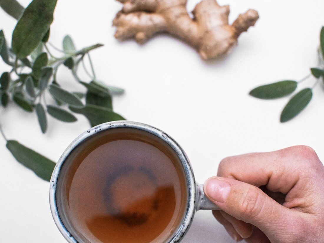 A hand holding a cup of sage and ginger tea (seen from above)