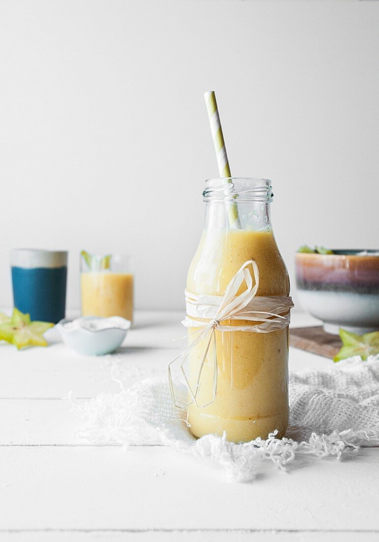 Mango and pineapple smoothie served in a glass bottle with a straw
