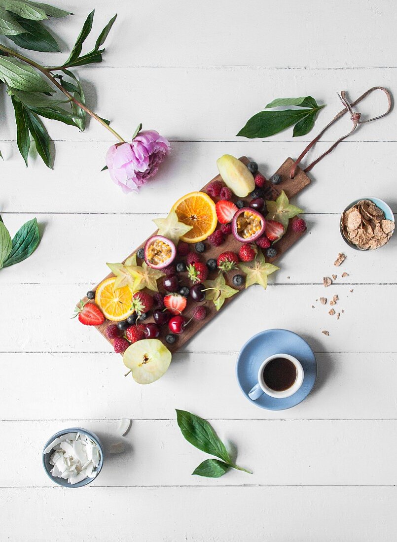Various fresh fruits served on a wooden board and a cup of coffee