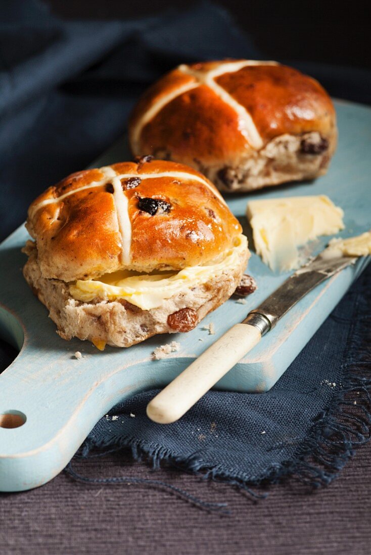 Hot cross buns with butter on a wooden chopping board (Easter baking, England)