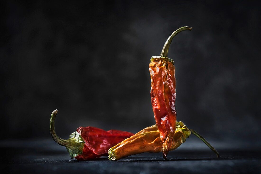 Three dried red chilli peppers in front of a black background