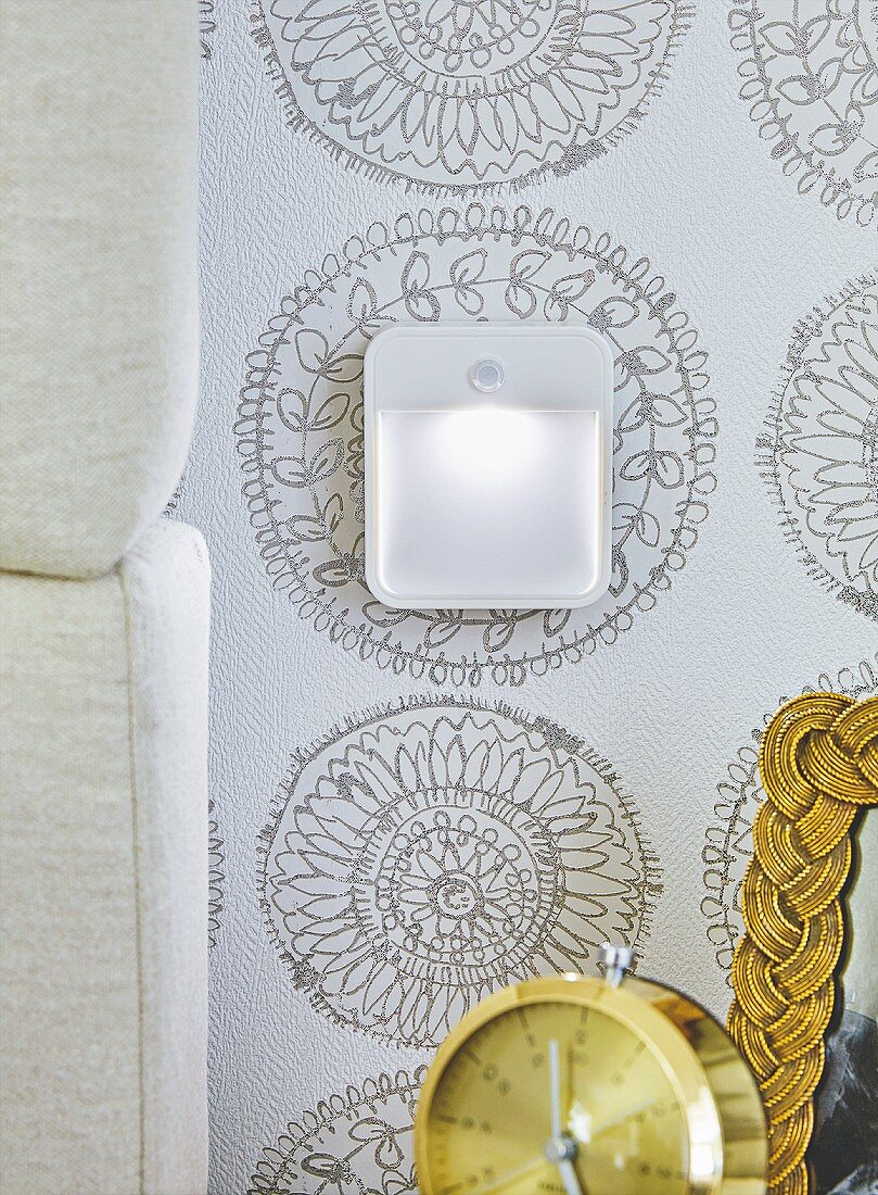 A night light on patterned wallpaper next to a headboard