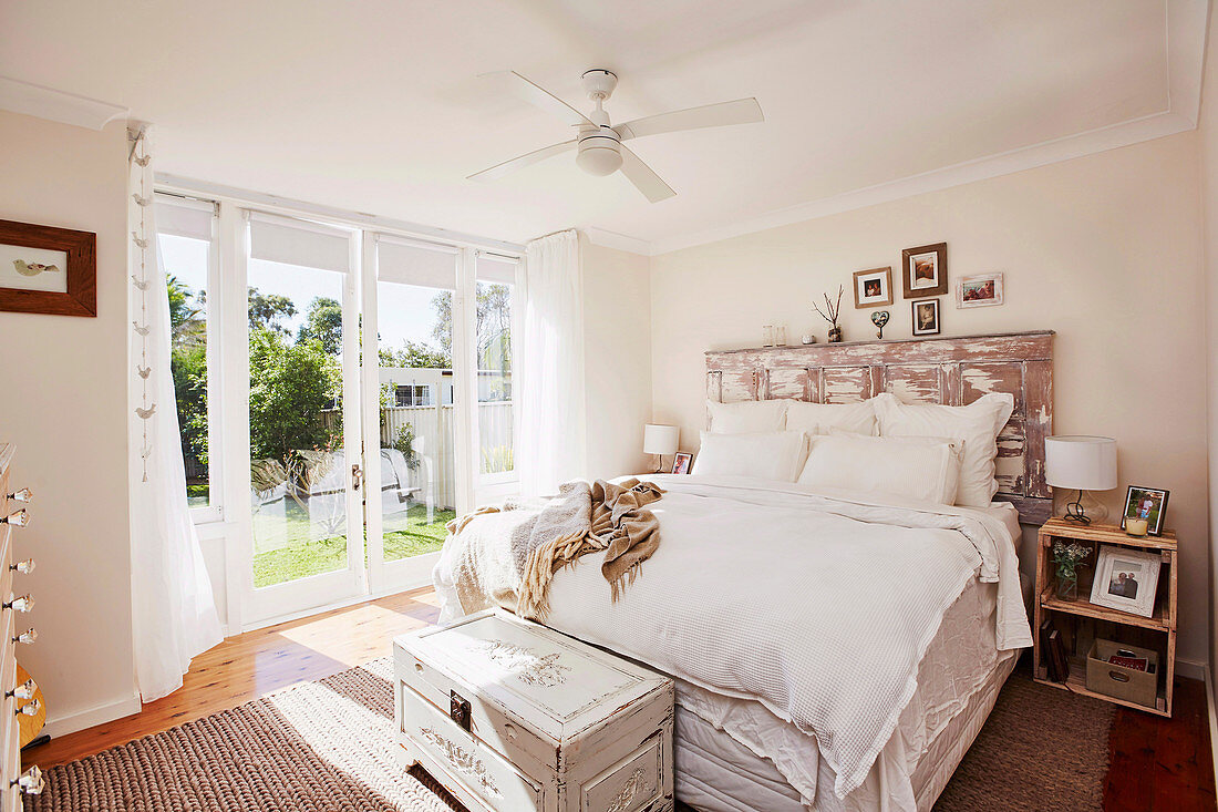 Double bed with DIY bed head from old wooden door in bright bedroom with garden access