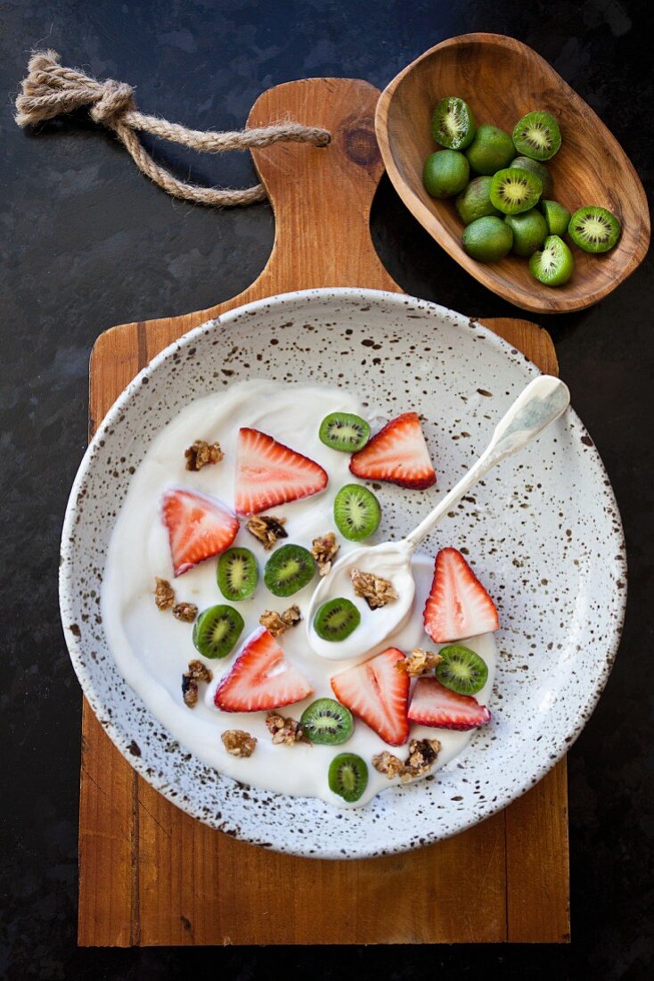 Vanilla yogurt with sliced strawberries and kiwi berries (mini kiwi), on a speckled plate on a wooden tray