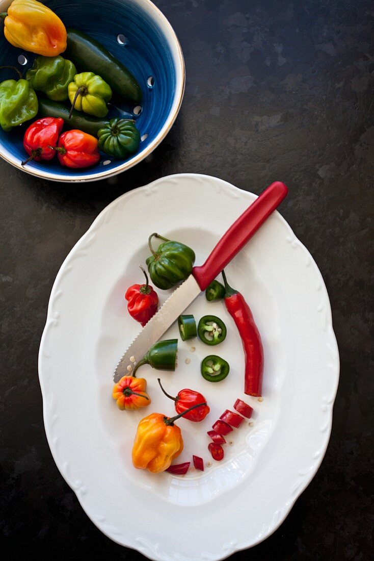 Various types of chili peppers, some sliced, on a white platter