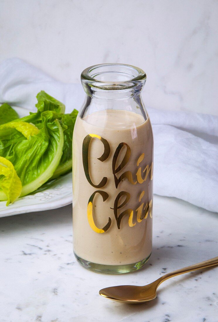 Eine Flasche Cäsarsalat-Dressing vor Romanasalat