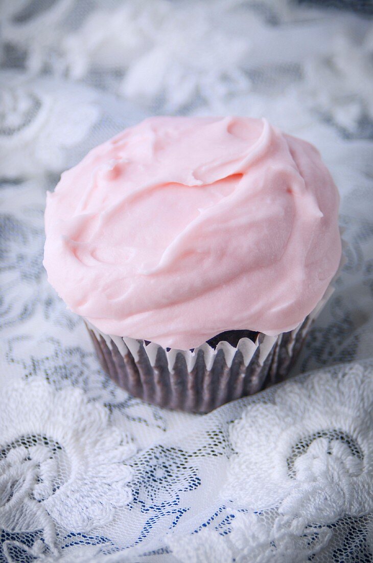 A Single Chocolate Cupcake with Pink Buttercream Frosting on a Lace Napkin
