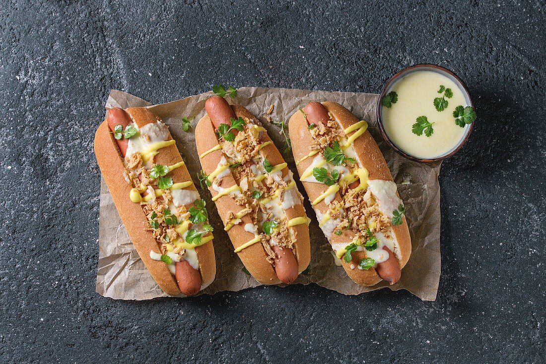 Hot Dogs mit Röstzwiebeln, Käsesauce, Senf und Koriander