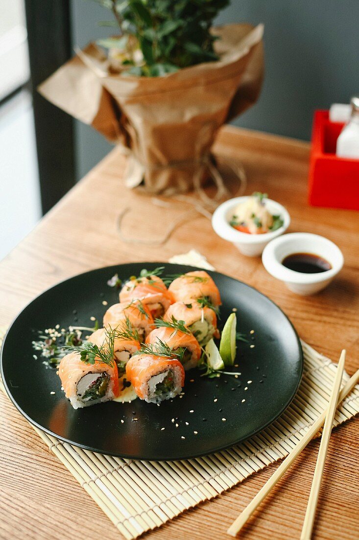 Sushiröllchen mit Lachs, Frischkäse und Kräutern auf schwarzem Teller