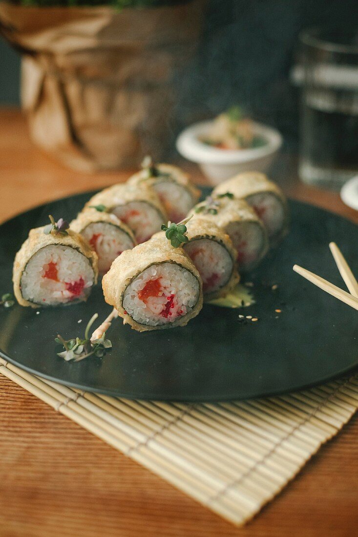 Sushi rolls with salmon, deep fried in tempura batter, on a black plate