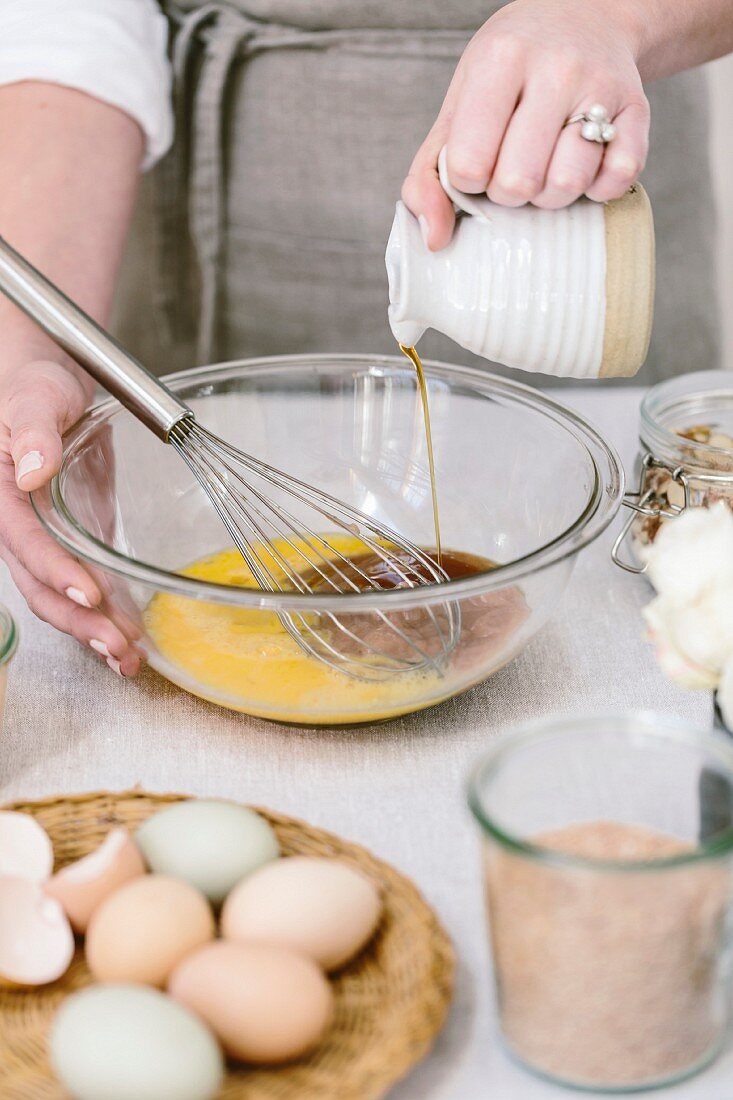 A woman is pouring maple syrup into an egg mixture as prep for a muffin mix