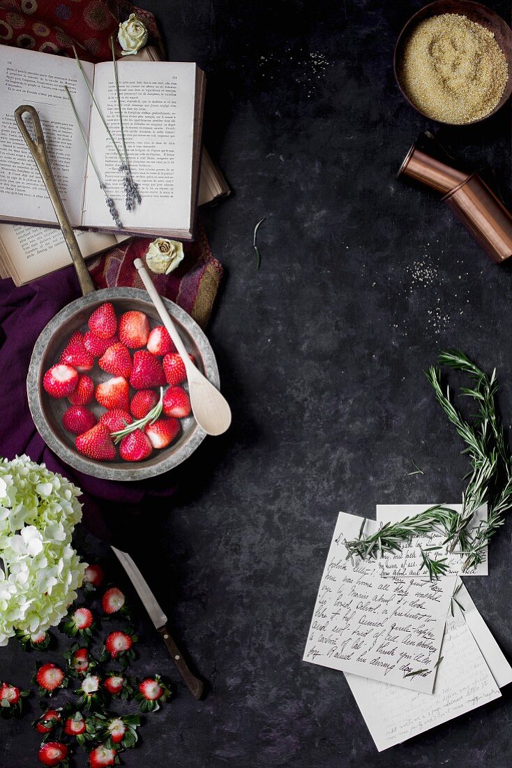 Stillleben mit entstielten Erdbeeren, Büchern, Briefen, Blüten und Rosmarin