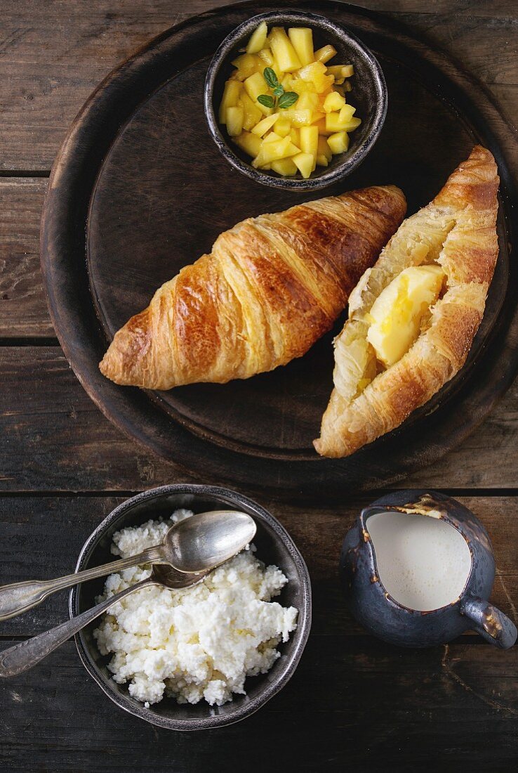 Breakfast with two croissant, butter, cottage cheese, cream and sliced mango fruit