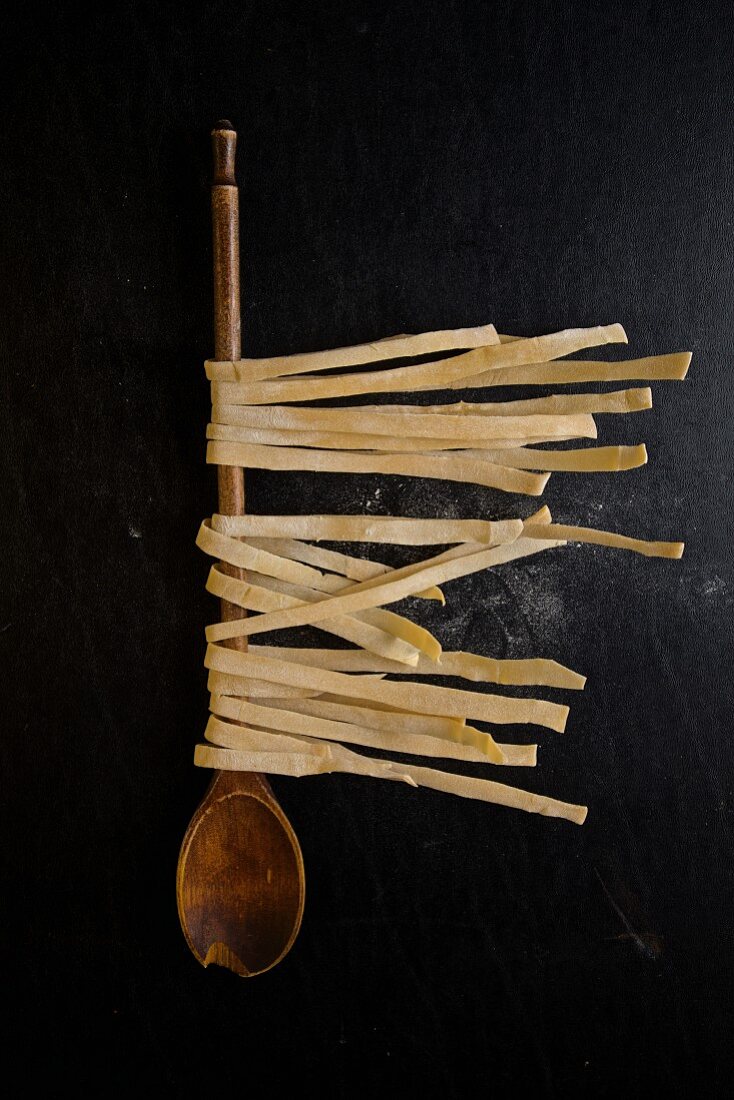 Homemade ribbon noodles hang over wooden spoons to dry