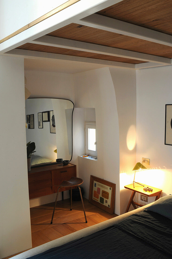 View across bed to lamp on bedside table, 50s dressing table with curved mirror and stool