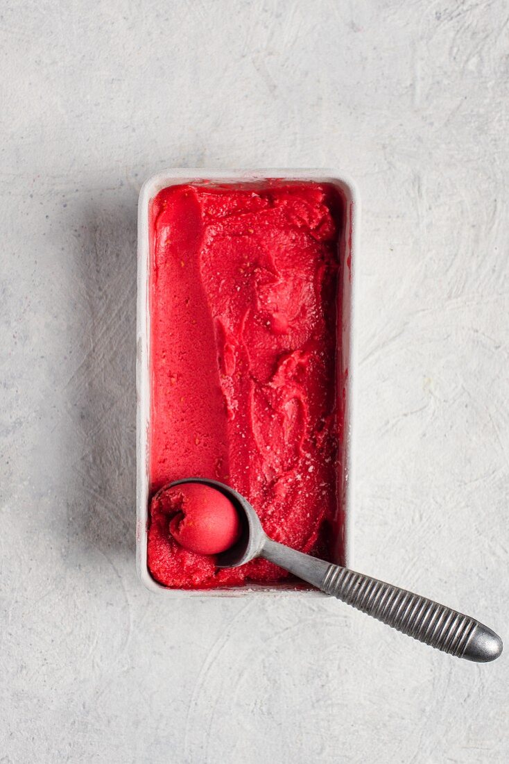 Raspberry sorbet with an ice cream scoop in a plastic dish (top view)