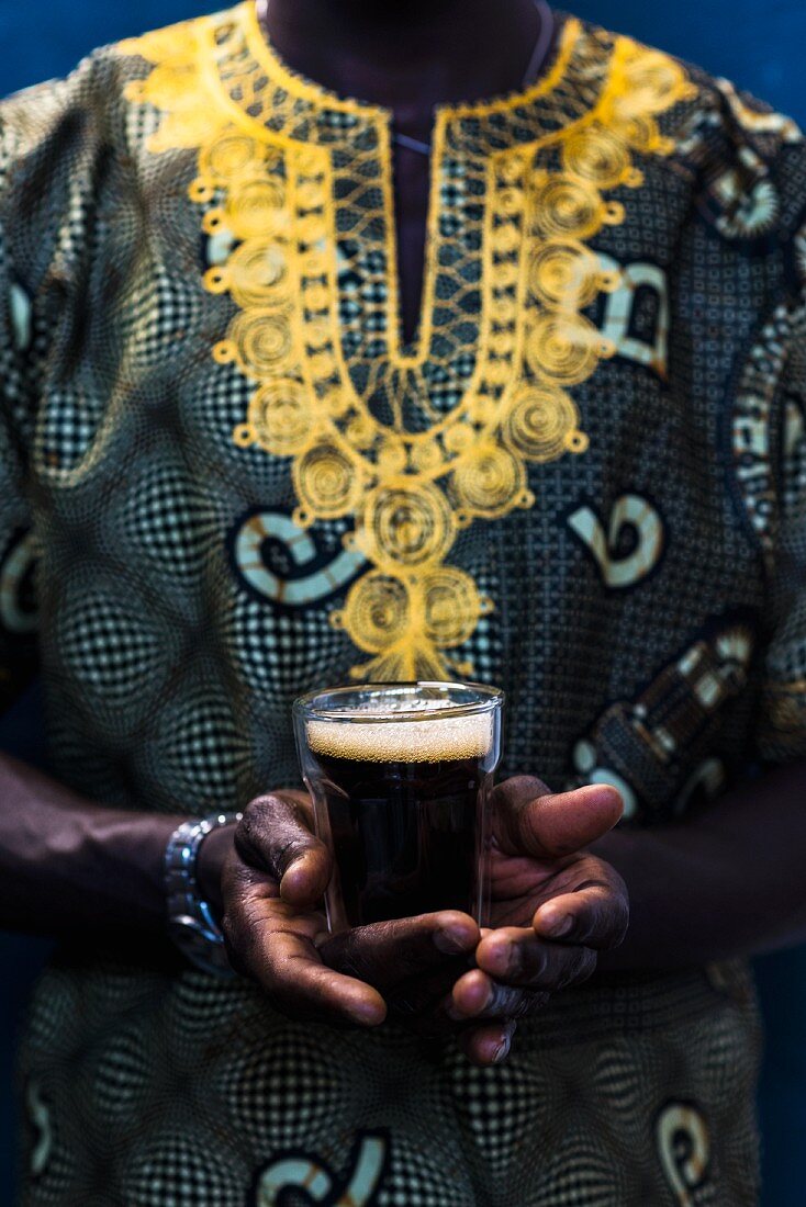 A Senegalese man in a traditional Boubou holds a glass of Touba (coffee drink, Senegal, Africa)