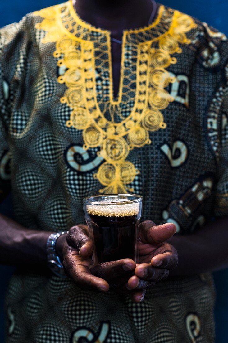 Senegalese in traditionellem Boubou hält ein Glas Touba (Kaffeegetränk, Senegal, Afrika)