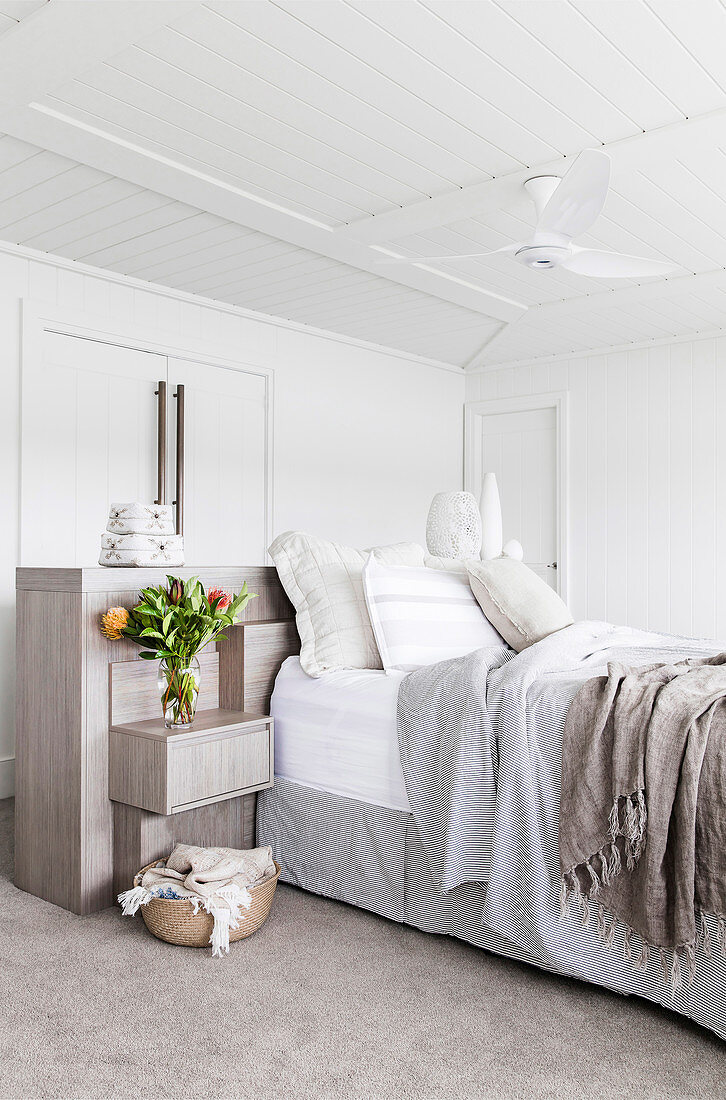 Bed head made of wood with integrated bedside cabinet on a double bed in a white bedroom