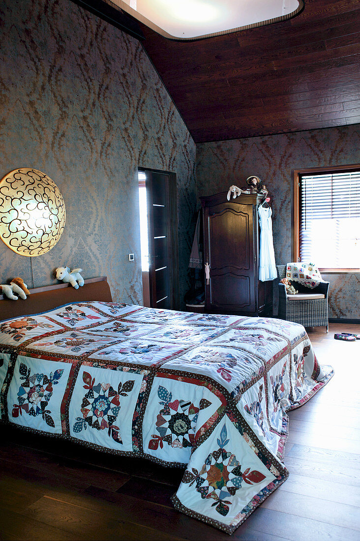 Quilt on bed in bedroom with dark ornate wallpaper