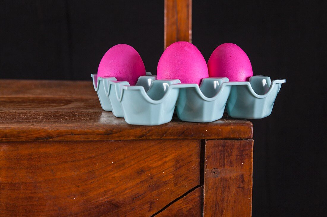 Pinke Ostereier im Eierkarton auf Holzstuhl