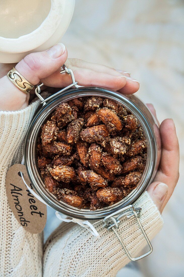A woman's hands holding a flip-top glass jar of Christmas almonds (seen from above)