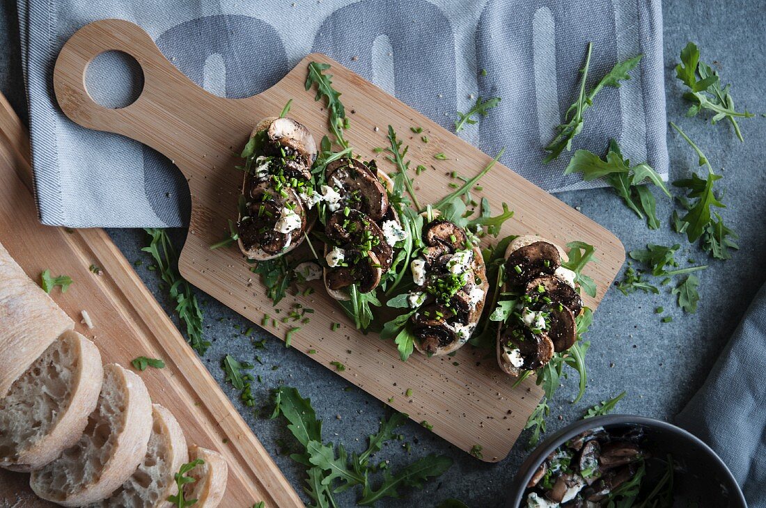 Bruschetta mit Pilzen, Feta und Rucola auf Holzschneidebrett (Aufsicht)