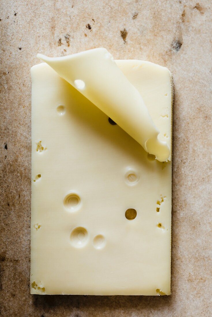 Slices of cheese with holes lying flat on a cream marble surface