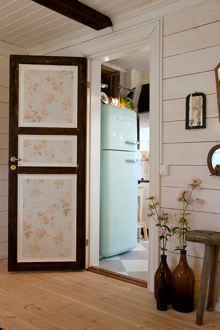 Panelled door with floral wallpaper leading into kitchen