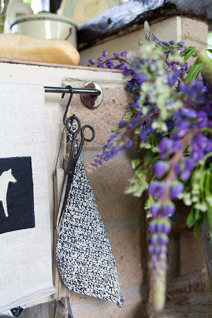 Scissors and crocheted pot holder next to blue lupins in kitchen