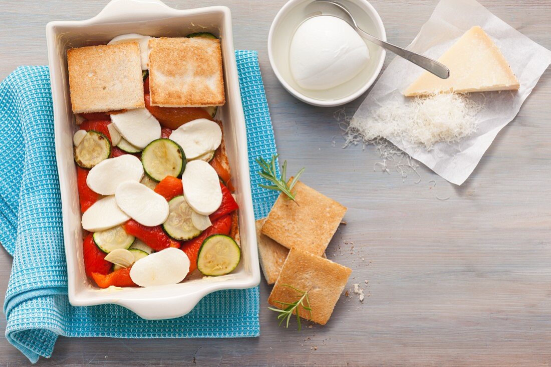 Toast and vegetables being layered into an ovenproof dish for vegetable gratin