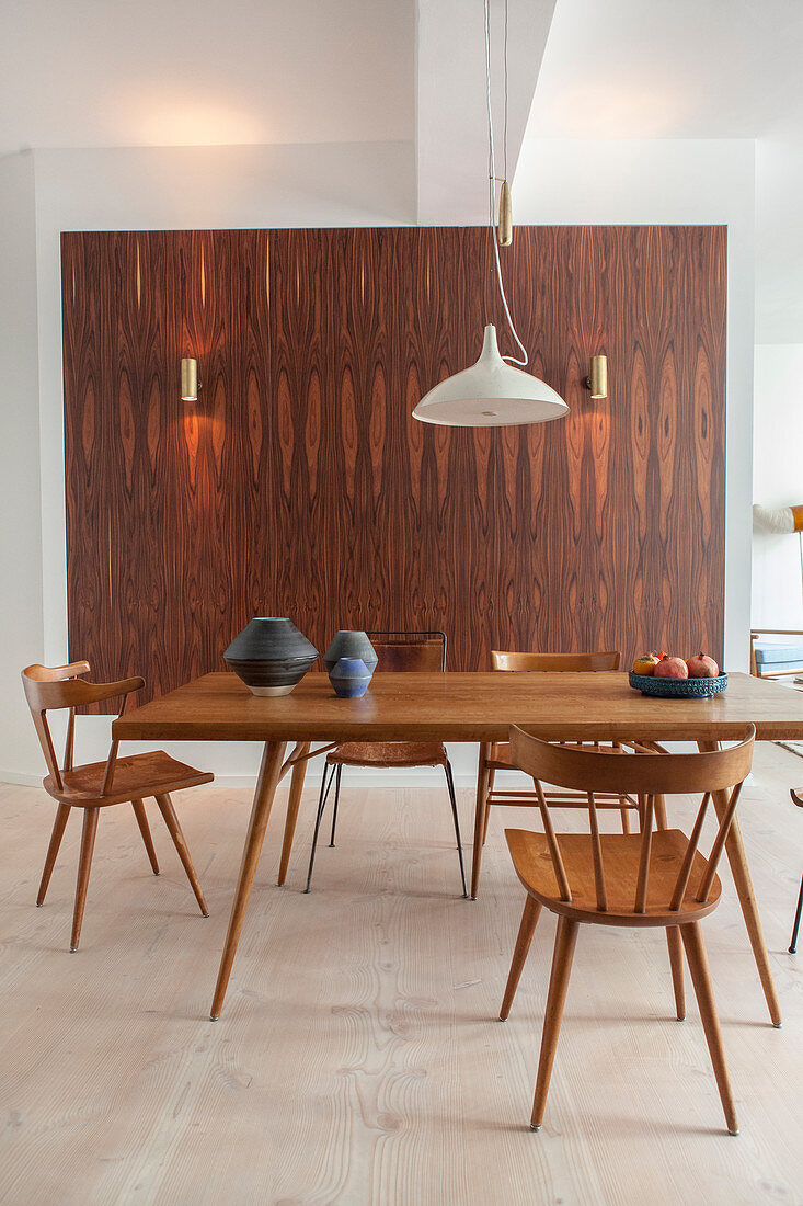 Various wooden chairs and dining table in front of wood-clad wall