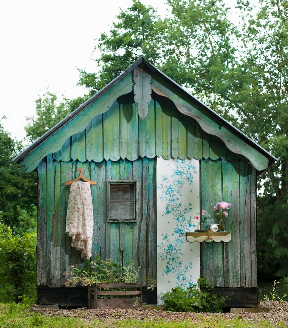 Weathered wooden hut decorated with strip of floral wallpaper, fabric and flowers
