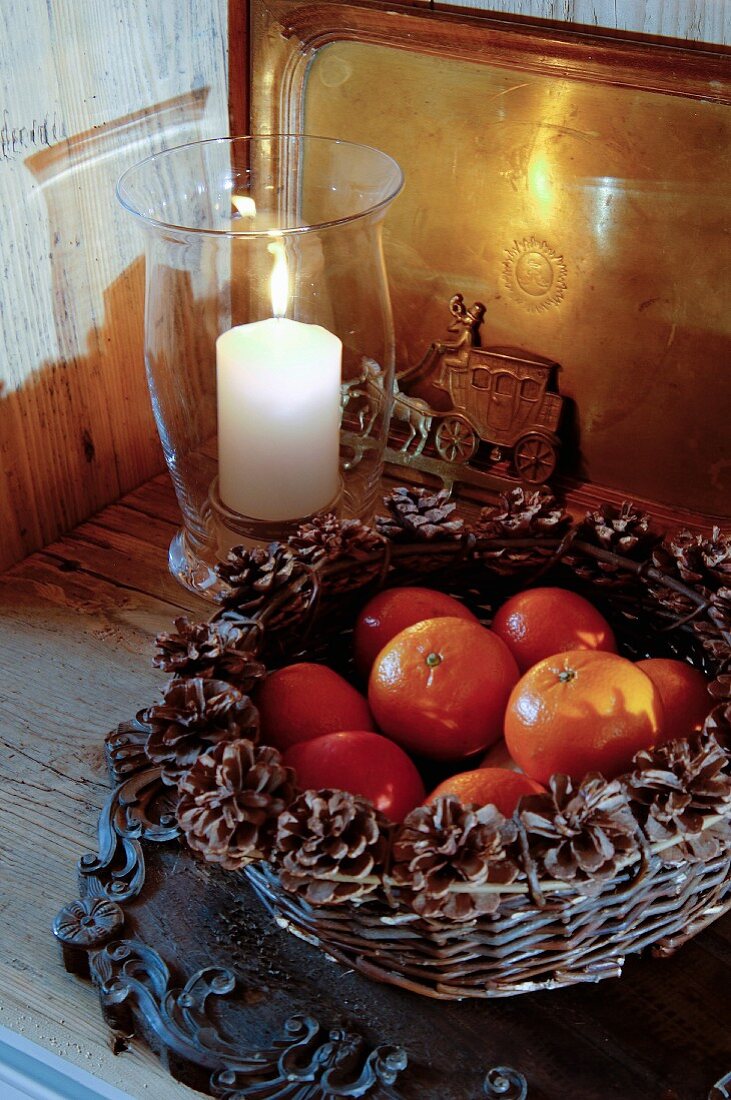 Basket of tangerines decorated with pine cones next to candle