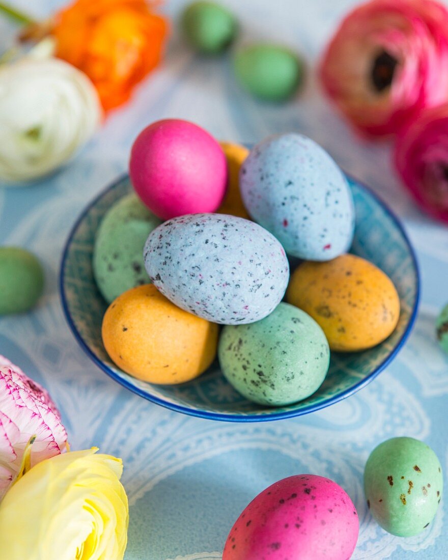 Bunte gesprenkelte Eier in Schale; Osterdekoration auf hellblauer Tischdecke