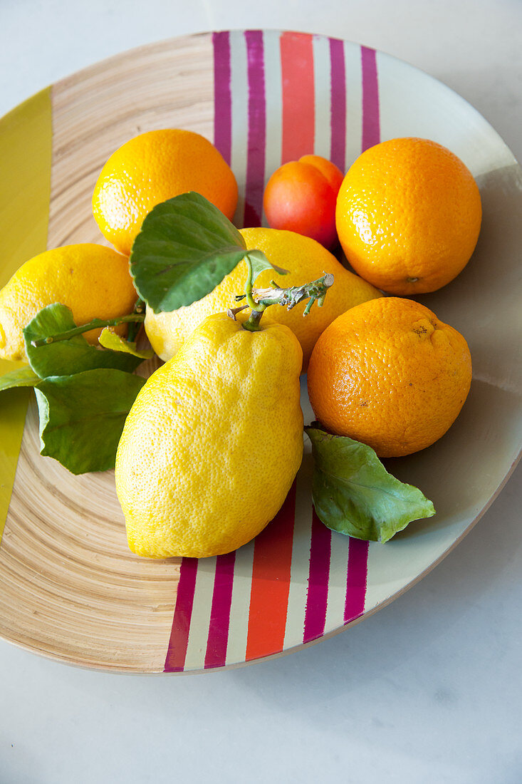 Citrusfrüchte auf einer Bambusschale mit bunten Streifen