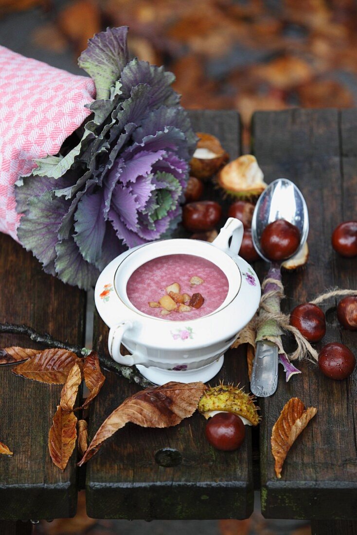 Rotkohlsuppe in kleiner Suppenterrine, daneben Kastanien und Herbstlaub