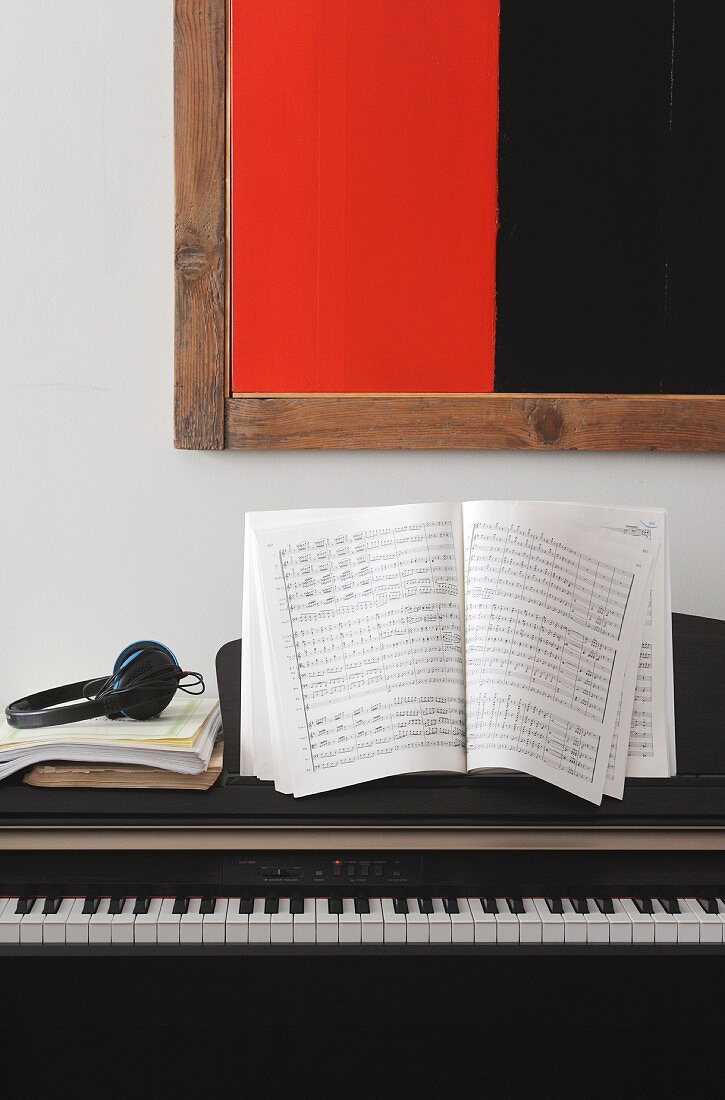 Sheet music and headphones on electric piano below black and red modern artwork