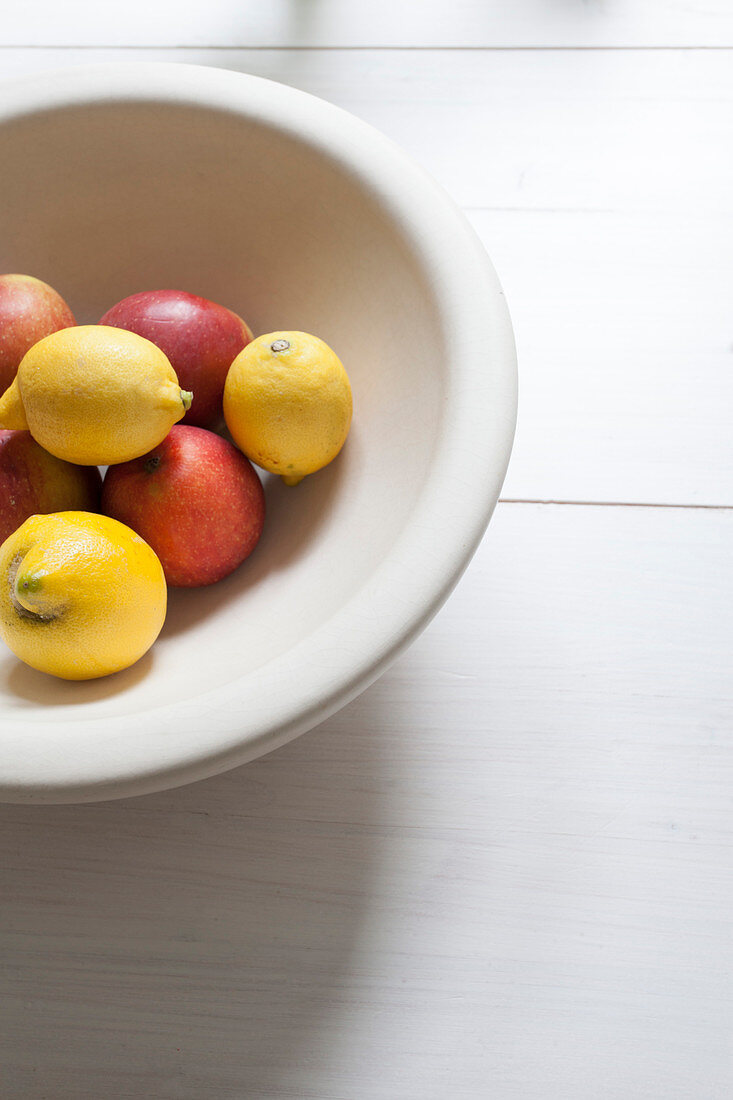 Zitronen und Äpfel in einer weißen Obstschale auf weißem Tisch