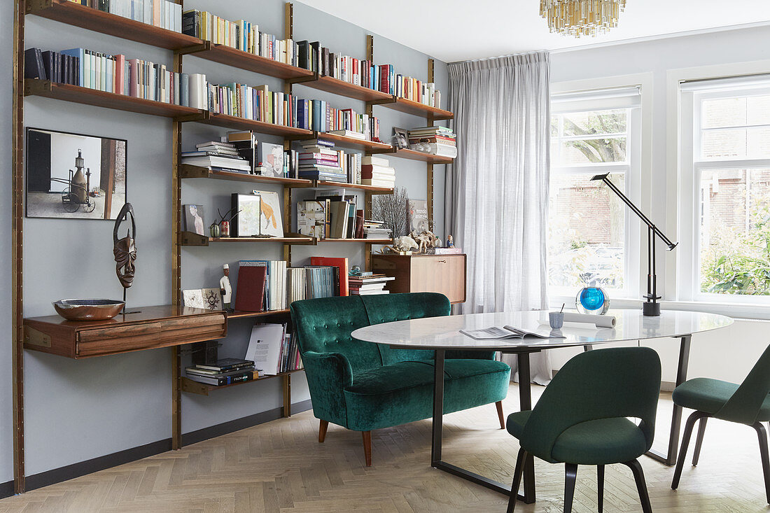 Sofa and upholstered chairs around oval dining room in front of wall-mounted shelving