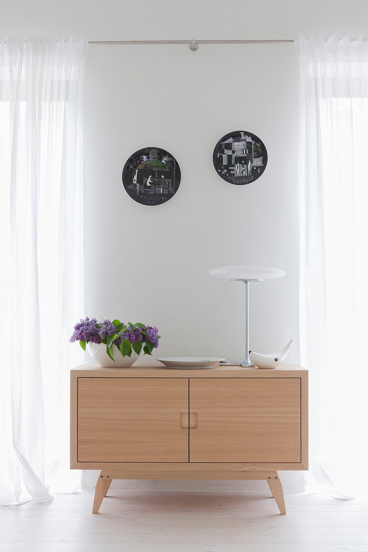 Sideboard aus hellem Holz im Retrostil zwischen zwei Fenstern