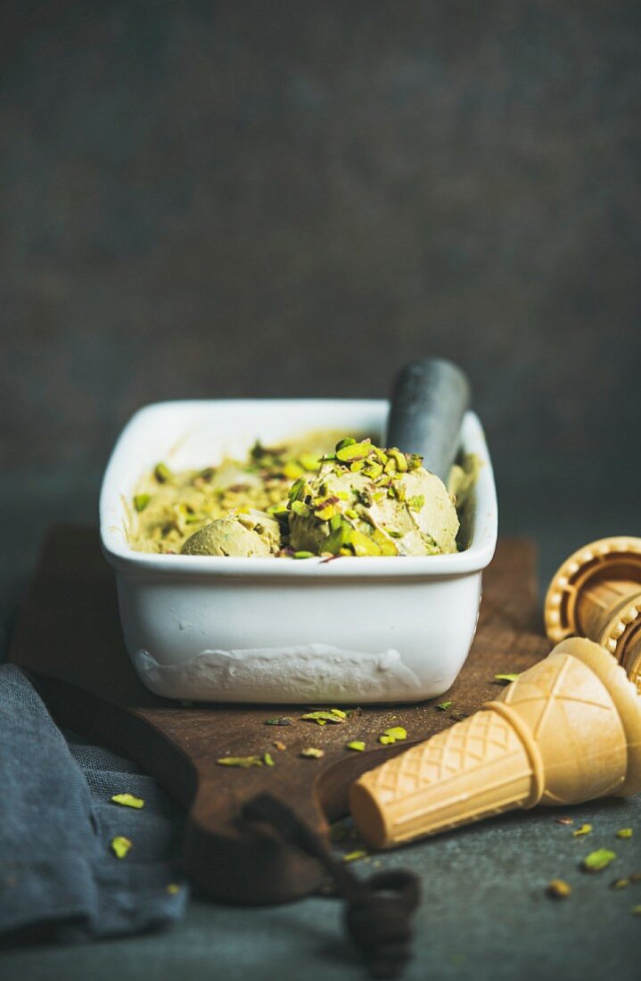 Homemade pistachio ice cream in ceramic mold with metal scooper, crashed pistachio nuts and waffle cones