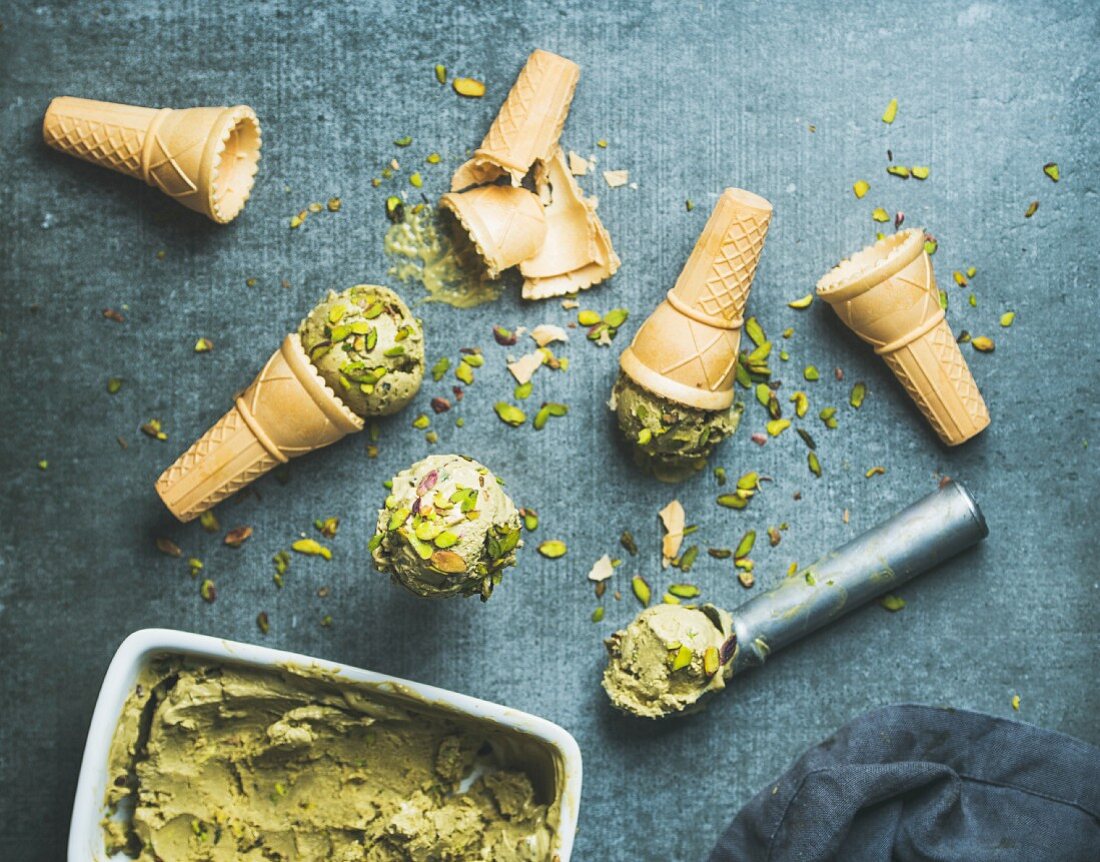 Homemade pistachio ice cream in ceramic mold and metal scooper with crashed pistachio nuts and waffle cones